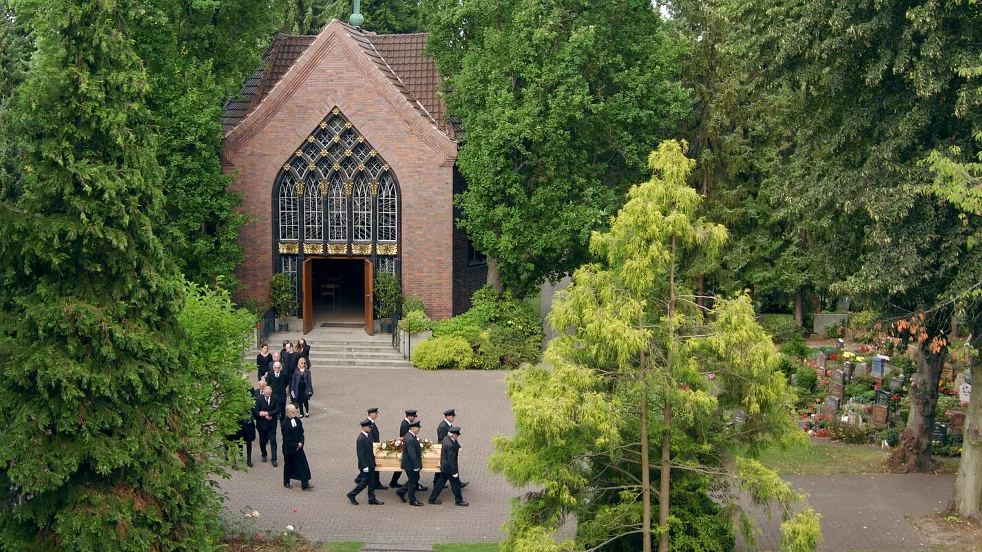 Friedhofskapelle vor der ein kleiner Trauermarsch stattfindet.