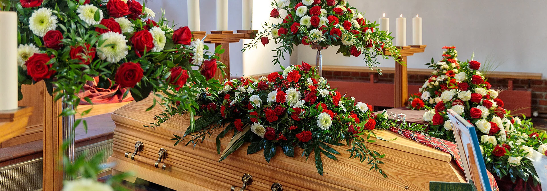 Sarg in Trauerhalle mit Blumenschmuck und Kerzen.