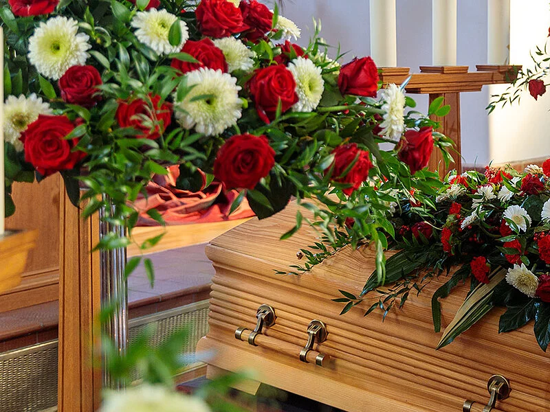 Sarg in Trauerhalle mit Blumenschmuck und Kerzen.