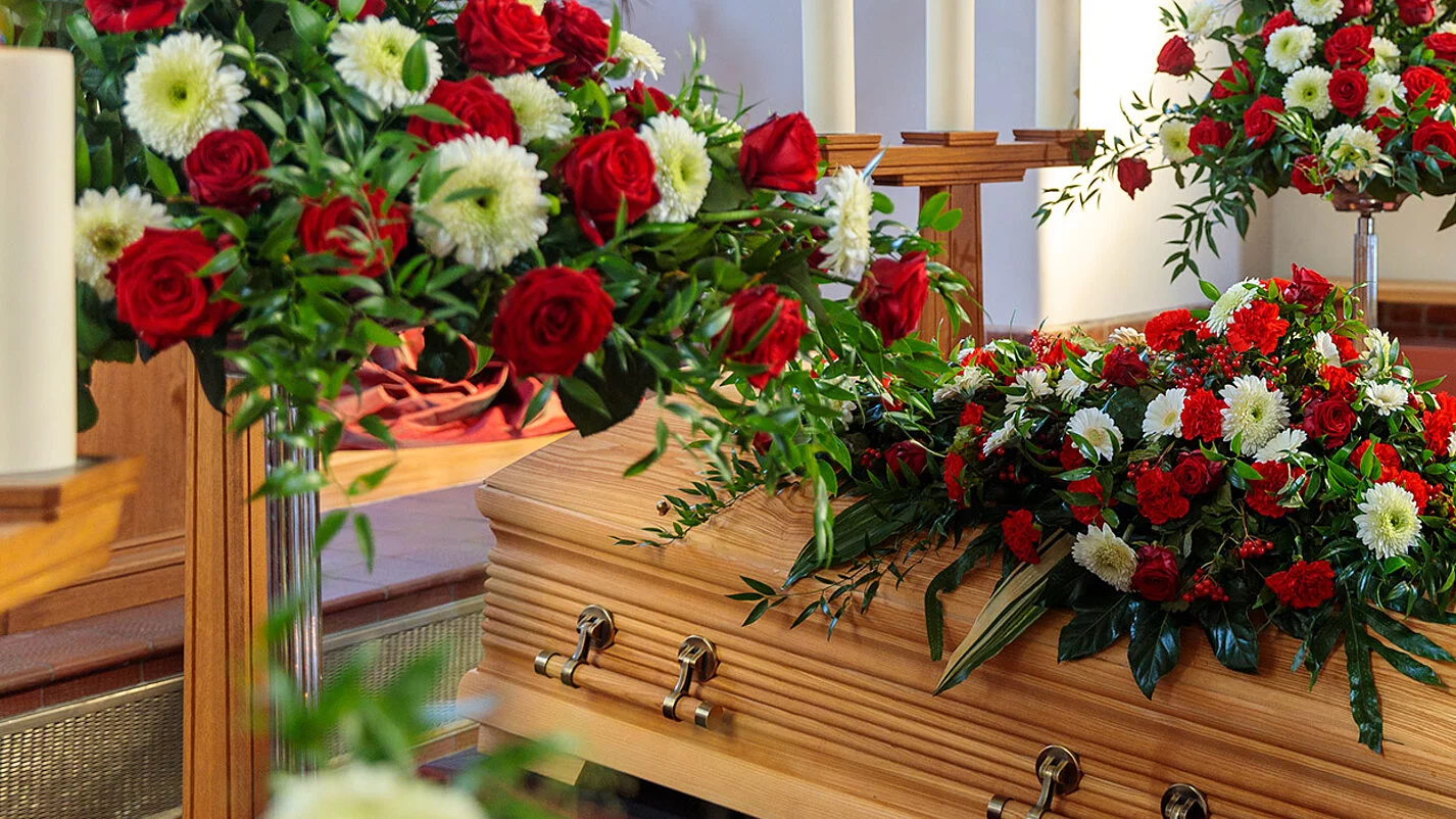 Sarg in Trauerhalle mit Blumenschmuck und Kerzen.