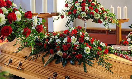 Sarg in Trauerhalle mit Blumenschmuck und Kerzen.