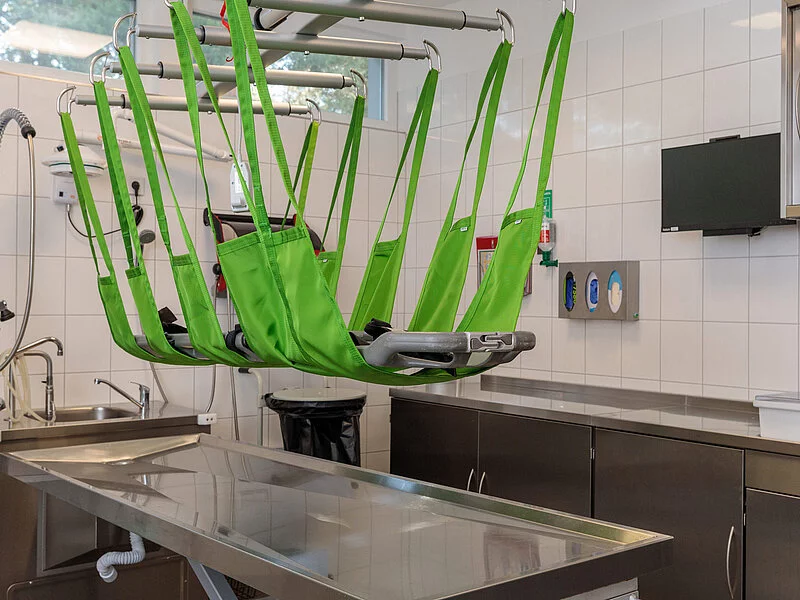 An Seilen befestigte Einbalsamierungsliege über einem Metalltisch.