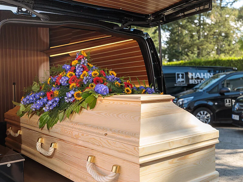 Sarg mit Blumenschmuck auf der Ladefläche eines Leichenwagens.