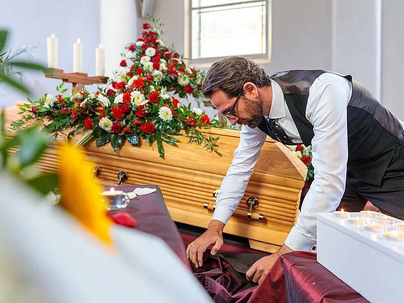 Bestatter richtet roten Samt für eine geschlossene Aufbahrung.