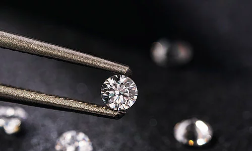 Ein Diamant wird von einer goldenen Pinzette in die Kamera gehalten.