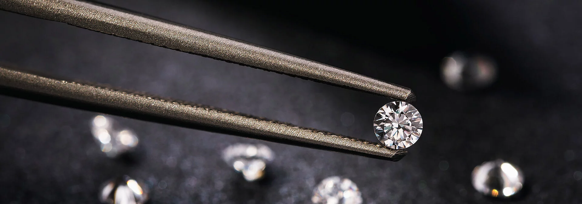 Ein Diamant wird von einer goldenen Pinzette in die Kamera gehalten.