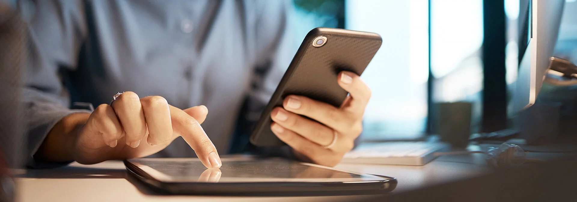 Person hält ein Handy in der linken Hand, und wischt mit der rechten auf einem Tablet.