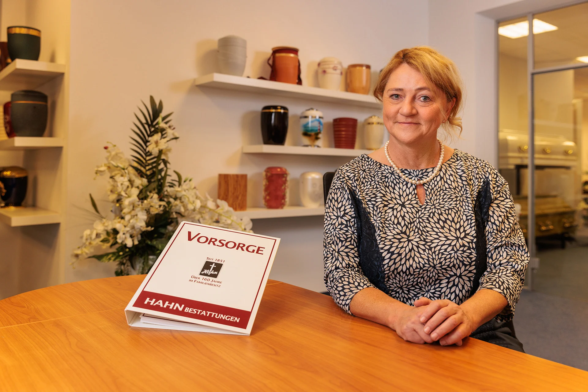 Frau an einem Holztisch stehend, neben Ihr ein Vorsorgeordner.